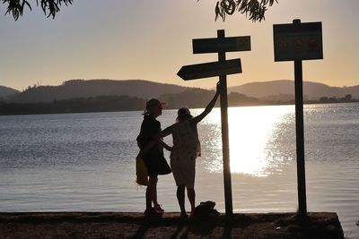 People standing on beach against sky during sunset