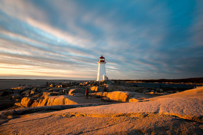 Lighthouse on rock against cloudy sky during sunset