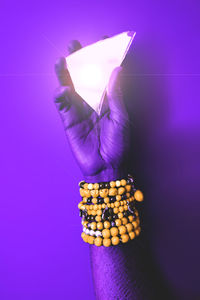 Cropped hand of man holding a mirror shape against purple background