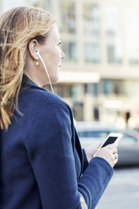 Businesswoman listening to music through headphones using mobile phone on street