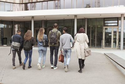 Rear view of multi-ethnic students walking against building in high school campus