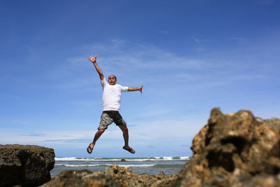 Full length of man jumping on rock at beach against sky