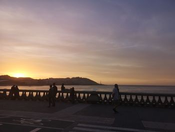 Silhouette people standing by sea against sky during sunset