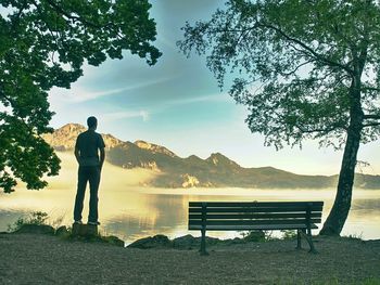 Alone man sits on bench beside an azure mountain lake. man relax bellow peaks of alps at lake 