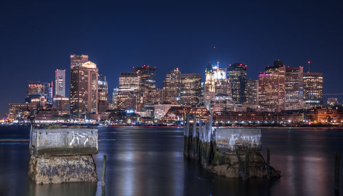 Illuminated buildings by river against sky at night