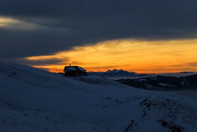 Snow covered landscape against sky during sunset