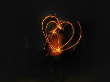 Man making heart shape light painting from sparklers at night