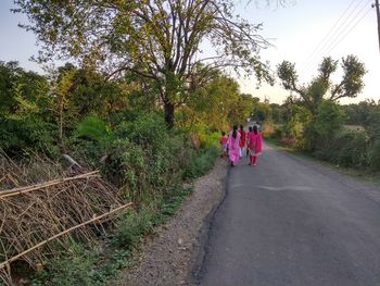 Rear view of people walking on road amidst trees