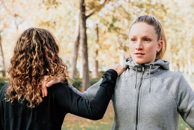 Woman standing with friend against tree