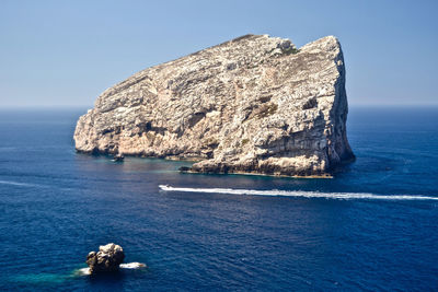 Rock formations in sea against clear blue sky