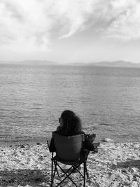 Rear view of woman sitting at beach against sky