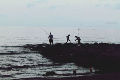 Silhouette men fishing in sea against sky