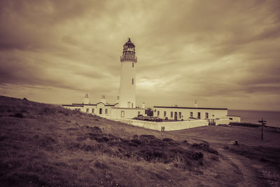 Lighthouse on field by building against sky