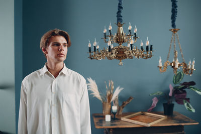 Man looking away while standing against chandelier