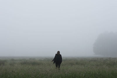 Woman walking amidst grassy field during foggy weather