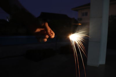 Cropped hand holding lit sparkler at night