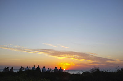 Silhouette people standing on shore against sky during sunset