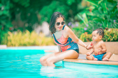 Smiling mother with son sitting by swimming pool