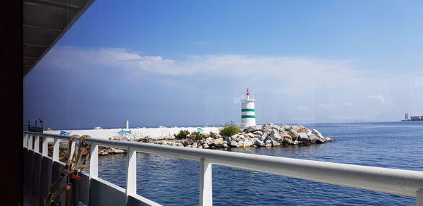 Lighthouse amidst sea and buildings against sky