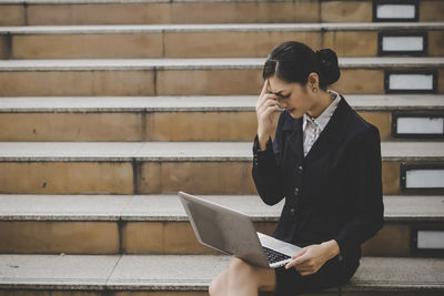 Businesswoman using laptop while sitting on steps in city
