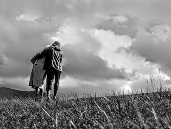 Rear view of man walking on field against sky