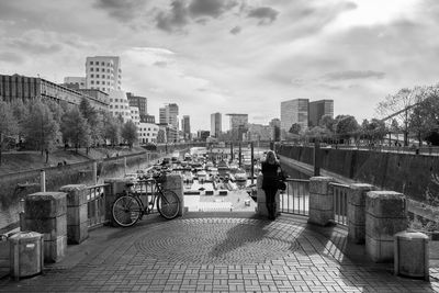 Rear view of woman standing at harbor against cloudy sky in city