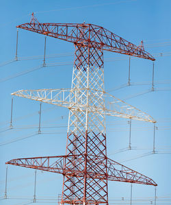 Low angle view of electricity pylon against clear blue sky