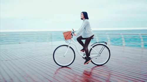 Woman riding bicycle on boat deck in sea against sky