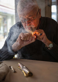 Senior man wearing eyeglasses smoking cigar sitting at table