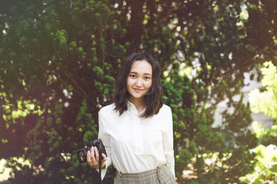 Optimistic asian young woman in a park holding camera, outdoor portrait. summer time 