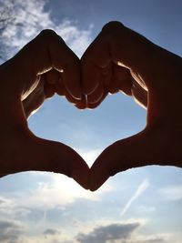 Cropped hands making heart shape against sky during sunset