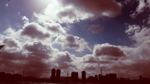 Silhouette cityscape against cloudy sky