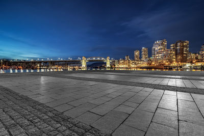 Illuminated city by street against sky at night