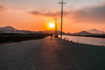 Man on road by sea against sky during sunset