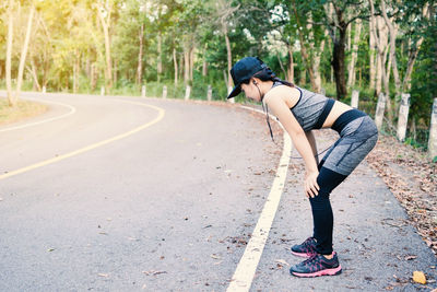 Full length of woman resting by road while exercising