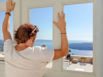 Rear view of man standing at window looking scenic nature