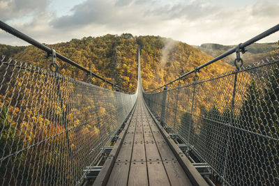Footbridge in forest against sky