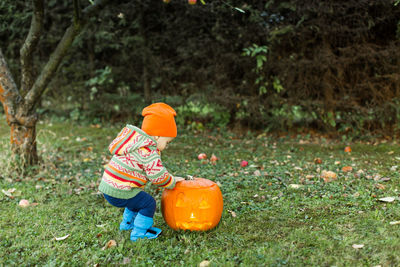 Full length of boy touching illuminated jack o lantern on grassy field