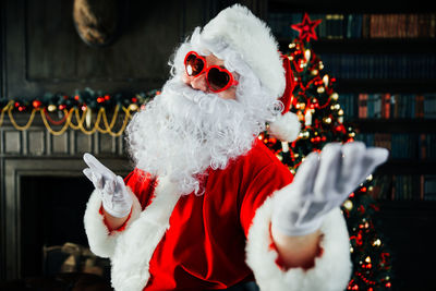 Portrait of santa clause wearing sunglasses standing against illuminated christmas tree