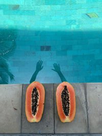 Shadows of hands on the water in the pool and cut papaya