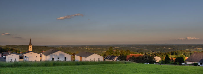 Houses on field by buildings against sky during sunset