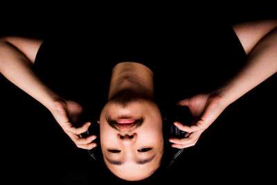 Upside down portrait of man wearing headphones against black background