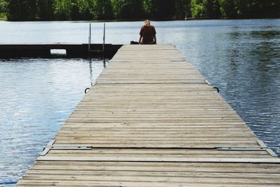 Rear view of woman sitting at the edge of pier over lake