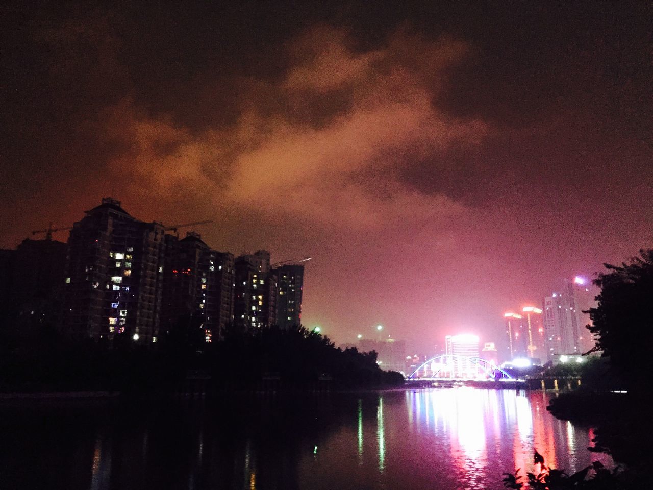 illuminated, city, building exterior, water, night, sky, architecture, built structure, cityscape, waterfront, reflection, skyscraper, river, urban skyline, cloud - sky, modern, city life, outdoors, no people, dusk