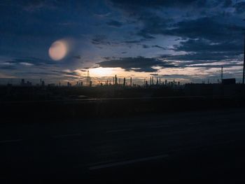 Silhouette road by buildings against sky at sunset