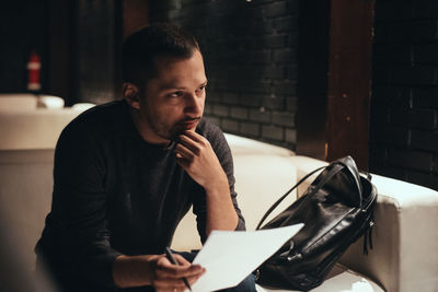 Thoughtful young man looking away while holding paper