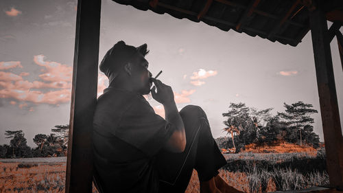 Man smoking cigarette against sky during sunset