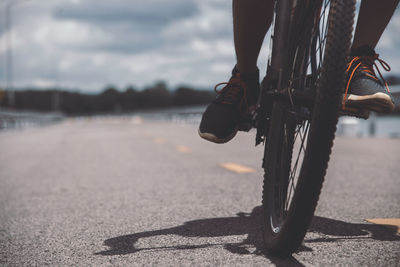 Low section of person with bicycle on shore against sky