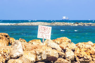Information sign on rock by sea against sky