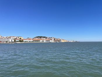 Sea by townscape against clear blue sky
